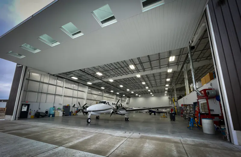 Bright maintenance hangar with its door open and a turboprop inside