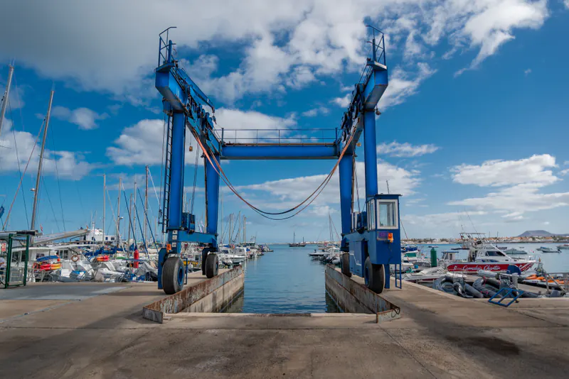 Blue travel lift straddling the haul-out slip at a sunny marina